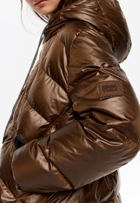 Brązowa puchowa kurtka z połyskującym wykończeniem, z kapturem, ukośnym pikowaniem i naszywką z logo na rękawie.