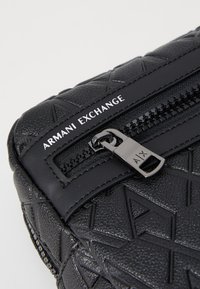 Borsa in pelle nera con texture, caratterizzata da motivi geometrici, chiusura a zip con hardware in metallo e dettaglio del logo impresso.
