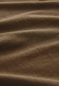 Barna pamutszövet sima textúrával, enyhe gyűrődéssel és redőkkel, közepes vastagságot és puha felületet mutatva.