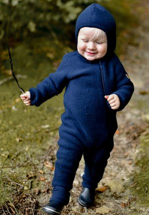 Navy blue, zippered fleece jumpsuit with a hood. Child holding a stick, wearing rubber boots, walking on a forest path. Textured surface.