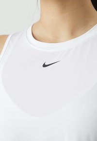 Gros plan du haut de la poitrine d'une personne portant un débardeur blanc de sport avec un logo Nike noir.