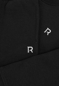 Hanorac negru, cu o textură moale a materialului, guler ribbinat și logo-ul alb brodat cu litera "R" pe piept și pe mânecă.