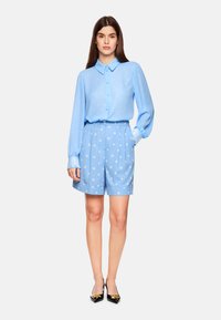Light blue blouse with button front and polka dot patterned shorts; features puff sleeves and lace accents on cuffs; paired with black heels.