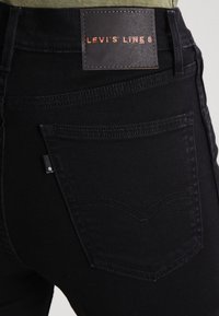 Svarta denimjeans med en läderlapp märkt "Levi's Line 8", bakfickor med böjd sömnad och subtila metalldetaljer.