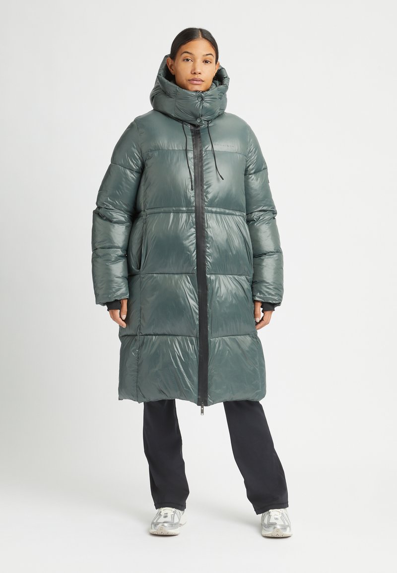 Gewatteerde lange jas in glanzend donkergroen met een hoge kraag, ritssluiting aan de voorkant en een oversized silhouet. Bevat elastische manchetten en zijzakken.