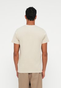 Μπεζ βαμβακερό μπλουζάκι με κοντά μανίκια και στρογγυλή λαιμόκοψη. Η πλάτη είναι απλή, με λείο υφή και άνετη εφαρμογή.