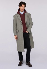 Šedý vlněný kabát s klopovým límcem, jednorezový, se třemi knoflíky. Kombinován s bordó mikinou s kapucí a černými kalhotami.