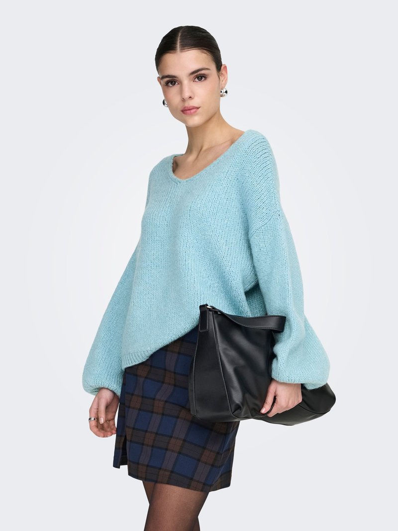 Vaaleansininen, ylisuuri neulepaita V-kaula-aukkolla ja teksturoidulla kankaalla; yhdistetty istuvaan ruudulliseen hameeseen ja mustaan nahkalaukkuun.