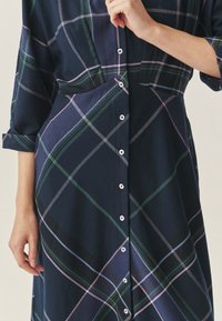 Navy kockás ruha zöld, rózsaszín és fehér vonalakkal. Gombos elülső rész gallérral és felgöngyölt ujjakkal. Puha anyag, laza szabással.
