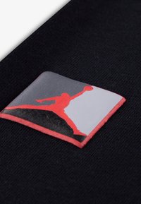 Μαύρο ύφασμα με ορθογώνιο μπαλώμα που έχει ένα κόκκινο και γκρι λογότυπο ενός ατόμου που πηδάει με μπάλα μπάσκετ, περιγραμμένο με κόκκινο.