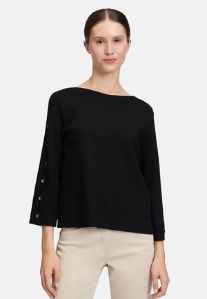 Maglione nero in maglia con scollo ampio, maniche 3/4 con polsini a costine e bottoni decorativi lungo il lato. Texture liscia.