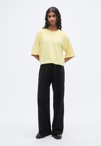 Haut jaune à manches courtes, coupe décontractée, en tissu doux, associé à un pantalon noir à jambes larges et des chaussures noires. Design simple sans motifs.