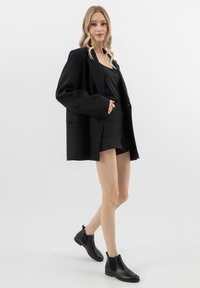 Czarna, oversize marynarka o eleganckim kroju, noszona na czarną bluzkę i krótką spódniczkę, w zestawieniu z czarnymi botkami do kostek. Gładki materiał, minimalistyczny design.