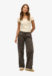 Hellbeige taillierter Oberteil mit Knöpfen und dunkelgraue Cargo-Hosen mit mehreren Taschen und verstellbaren Bündchen, kombiniert mit beigefarbenen Sneakers.