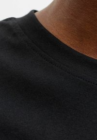 Juoda medvilnės marškinėlių medžiaga su lygiu paviršiumi, turinti giliai iškirptą, neryškias kaklo dalies siūles ir tvirtai austas siūles.