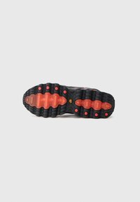 Sola de sapatilha preta com borracha texturizada, apresentando um padrão ondulado e detalhes em vermelho brilhante. Sulcos circulares e retangulares para melhor aderência.