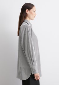 Chemisier à manches longues à rayures noires et blanches. Doté d'un col classique et de poignets boutonnés ; coupe ample ; texture de tissu lisse.