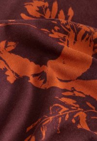 Puuvillane kangas tume burgundi alusega ja julge oranži lillemustriga, esitledes sujuvat tekstuuri ja keerukat detaili.