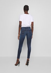 Vaqueros ajustados de mezclilla azul con cintura alta, acentos desgastados y dos bolsillos traseros. Combinados con una camiseta blanca sencilla y tacones negros.