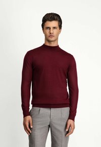 Burgundowa dzianinowa sweter z wysokim okrągłym dekoltem, długimi rękawami i dopasowaną sylwetką, w połączeniu z jasnoszarymi spodniami.