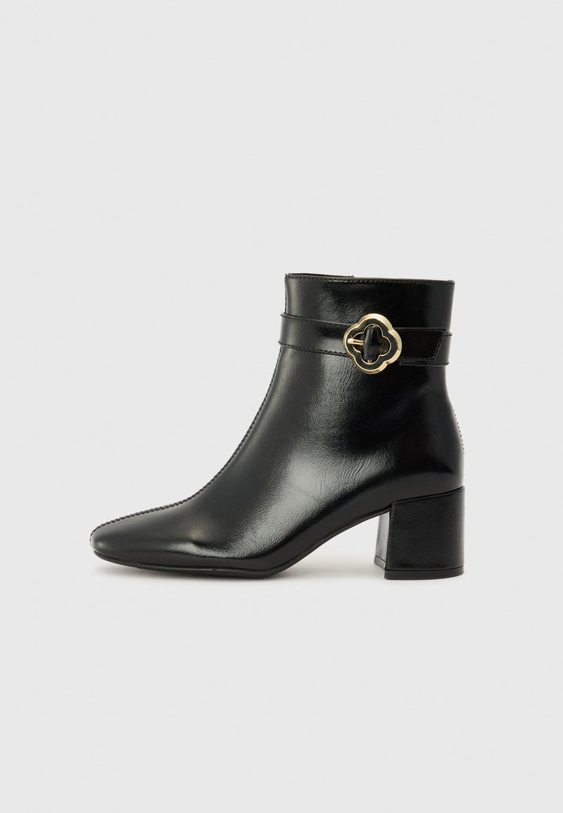 Bottine en cuir noir avec un bout pointu, un talon carré et des accents en métal doré. Texture lisse et éléments de design minimalistes.