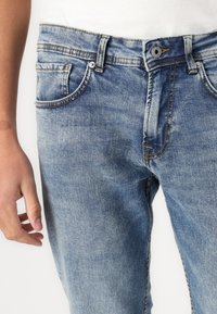 Hellblaue Denim-Jeans mit einem verblassten Finish, fünf Taschen-Design, kontrastierenden gelben Nähten und gesichertem Bund mit einem Metalldruckknopf.