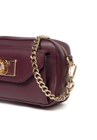 Burgundowa skórzana torebka o fakturowanej powierzchni, ze złotym łańcuszkiem oraz dekoracyjnym zapięciem z akcentem w postaci kamienia szlachetnego.