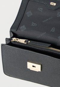 Μαύρη τσάντα χειρός από δερματίνη με υφή, με χρυσό κούμπωμα χαραγμένο με τη λέξη "Steve Madden", ανοιχτή για να φαίνεται η εσωτερική επένδυση και το φερμουάρ με χρυσή λαβή.