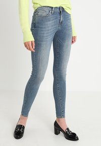 Smala blå jeans med en blekt tvätt, som har en traditionell femfickdesign och en slim fit. Bärs med svarta lackläderklackar.
