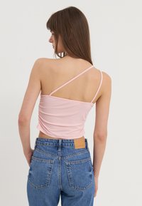 Top court ajusté rose avec une texture plissée et de fines bretelles réglables, associé à un jean en denim bleu taille haute avec une empiècement en cuir beige.
