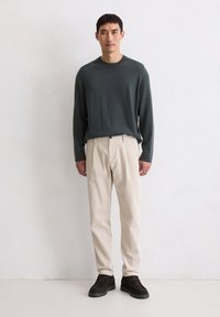 Chemise à manches longues de couleur vert foncé avec un col rond, accompagnée de pantalons en velours côtelé beige clair et de chaussures en daim marron foncé. Design simple, sans motifs.