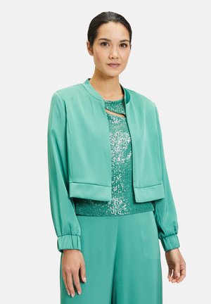 Tiefgrüne, taillierte Jacke mit langen Ärmeln und Rundhalsausschnitt, kombiniert mit einem schimmernden, grünen Paillettenoberteil. Glattes Material und figurbetontes Design.