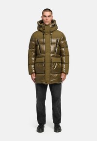 Olijfgroene pufferjack met een glanzende afwerking, voorzien van een capuchon, dubbele voorzakken en ritszakken op de borst. Zwarte accenten overal.