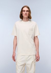 Beige bomull T-skjorte med rund hals, korte ermer og en brystlomme med sydd merke. Glatt tekstur, avslappet passform.