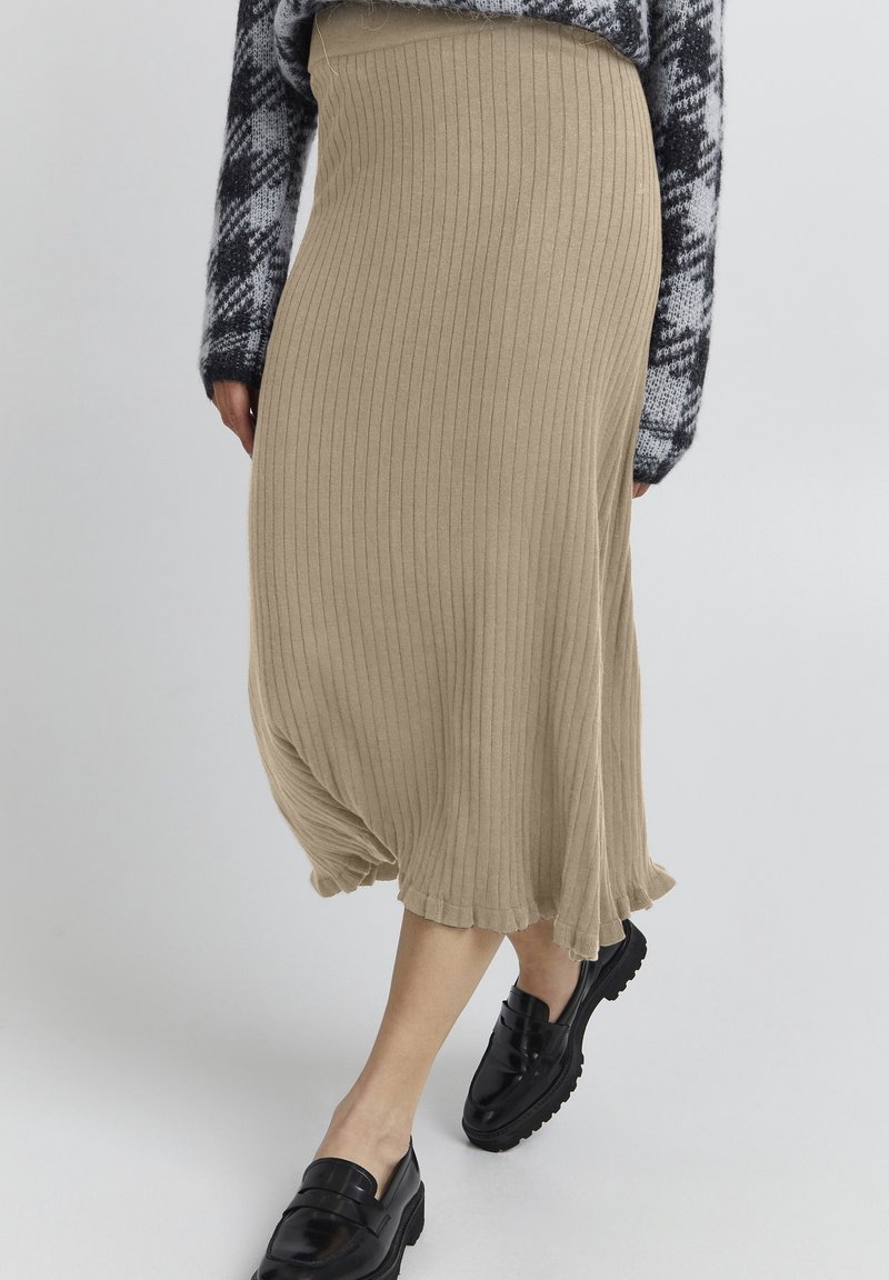Jupe midi en maille côtelée beige avec ourlet à volants, portée avec des mocassins noirs et un pull à motifs noir et blanc.