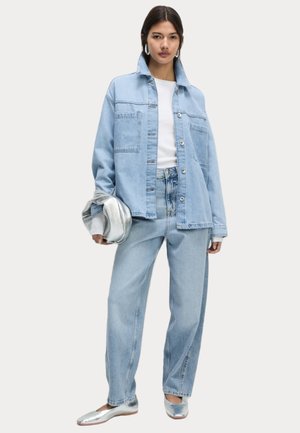 Light blue denim oversized jacket with button closure, paired with a white top and matching light blue jeans. Features silver flat shoes.