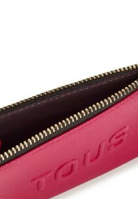 Bolso con cremallera de cuero rosa que presenta el logo embosado "TOUS", con herrajes de cremallera en tono dorado y un forro interior oscuro.