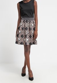 Zwarte mouwloze top gecombineerd met een geplooide A-lijn rok met een geometrische print in zwart en beige. De tailleband is grijs.