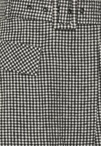 Svart och vit liten rutig tyg med en ficklock och fyra svarta knappar i en horisontell rad.