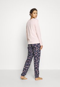 Lichtroze blouse met lange mouwen, gecombineerd met marineblauwe pyjamabroek met bloemenpatroon, voorzien van elastische manchetten. Zachte katoenen textuur, casual pasvorm.