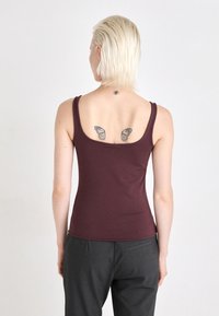 Top in borgogna con spalline sottili, design aderente e texture liscia, abbinato a pantaloni grigi a vita alta.