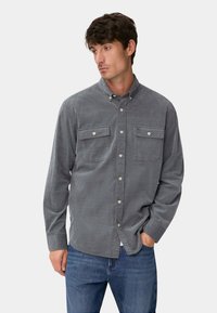 Graues Hemd mit strukturierter Oberfläche, ausgestattet mit zwei Brusttaschen und einem Kragen, kombiniert mit blauen Jeans.