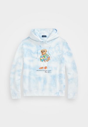 Sudadera con capucha de teñido anudado azul claro con un gráfico frontal de un oso con gafas de sol, camisa tropical, pantalones blancos y zapatos naranjas.