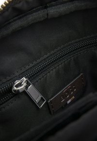 Inredningen av en svart nylonväska med ett fack med dragkedja, blank silverfärgad dragkedja och en brun läderetikett med präglad "BOSS"-logotyp.