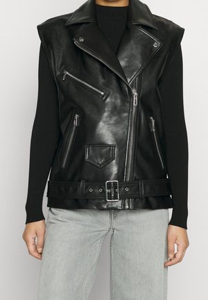 Gilet biker sans manches en similicuir noir avec fermeture éclair asymétrique, ceinture à la taille et poches zippées, porté sur un top noir à manches longues.