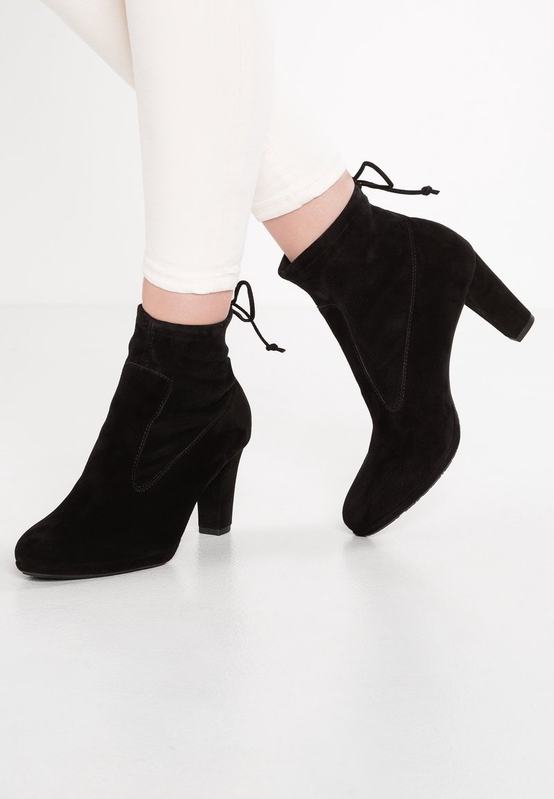 Černé kotníkové boty z broušené kůže s vysokým podpatkem, s špičatou špičkou a jedinečným zakřiveným výřezem na boku. Zavazují se na kotníku pro nastavitelný střih.