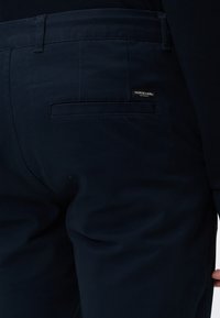 Pantalon bleu marine foncé avec passants de ceinture et une poche passepoilée à l'arrière, ornée d'une petite étiquette avec le logo Scotch & Soda Amsterdam.