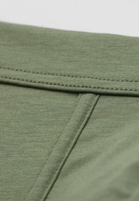 Tkanina w kolorze oliwkowym o gładkiej strukturze, z płaskim szwem i subtelnymi detalami przeszyć, podkreślająca jej lekką, codzienną konstrukcję.