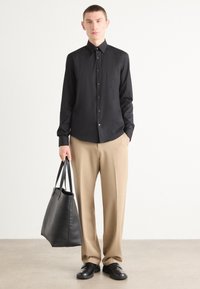 Zwarte overhemd met lange mouwen, beige broek en zwarte leren tas. Glad materiaal, getailleerde pasvorm en minimalistisch ontwerp.