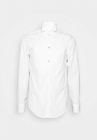Chemise blanche à manches longues, avec un front à boutons et un col. Elle présente un appliqué arrondi sur la poitrine et une texture en coton lisse.